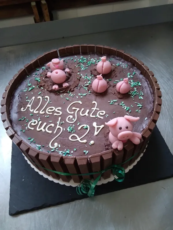 Schokoladen-Motivtorte mit Marzipanschweinchen und Schriftzug „Alles Gute euch 2“ aus der Konditorei von Mo's Café