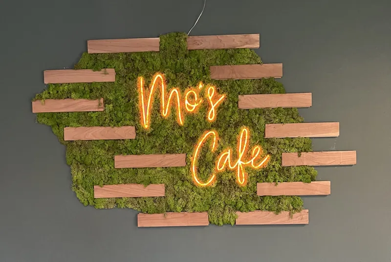 Leuchtschriftzug „Mo's Cafe“ auf einer Mooswand im Gastraum